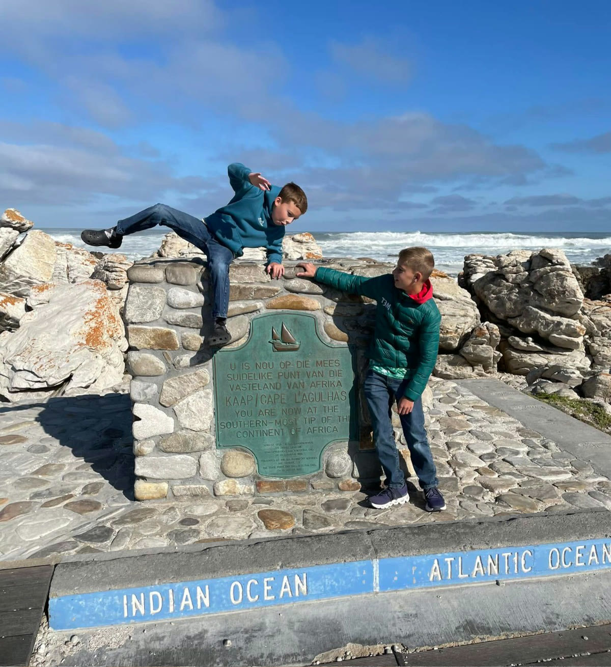 Two boys climbing the monument where the Indian and Atlantic Oceans meet